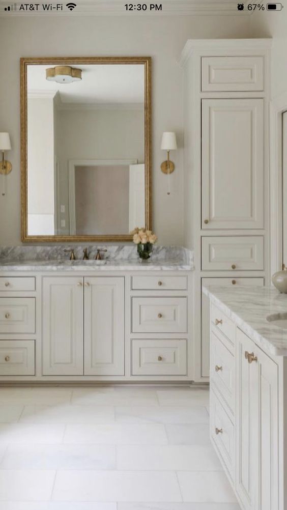 a large bathroom with white cabinets and marble counter tops, along with a gold framed mirror on the wall