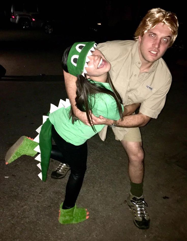 a man and woman in costume posing for a photo with a fake alligator on their head