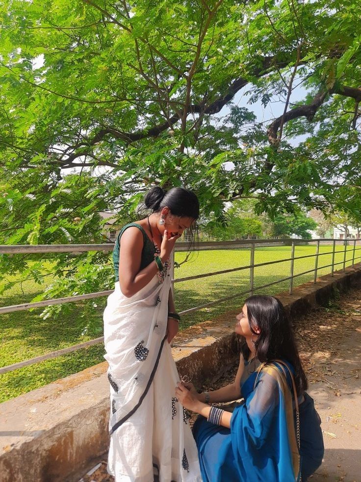 two women standing next to each other near a tree