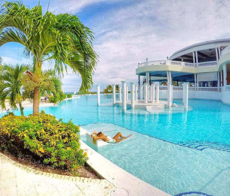 a woman laying on the edge of a swimming pool in front of a large building