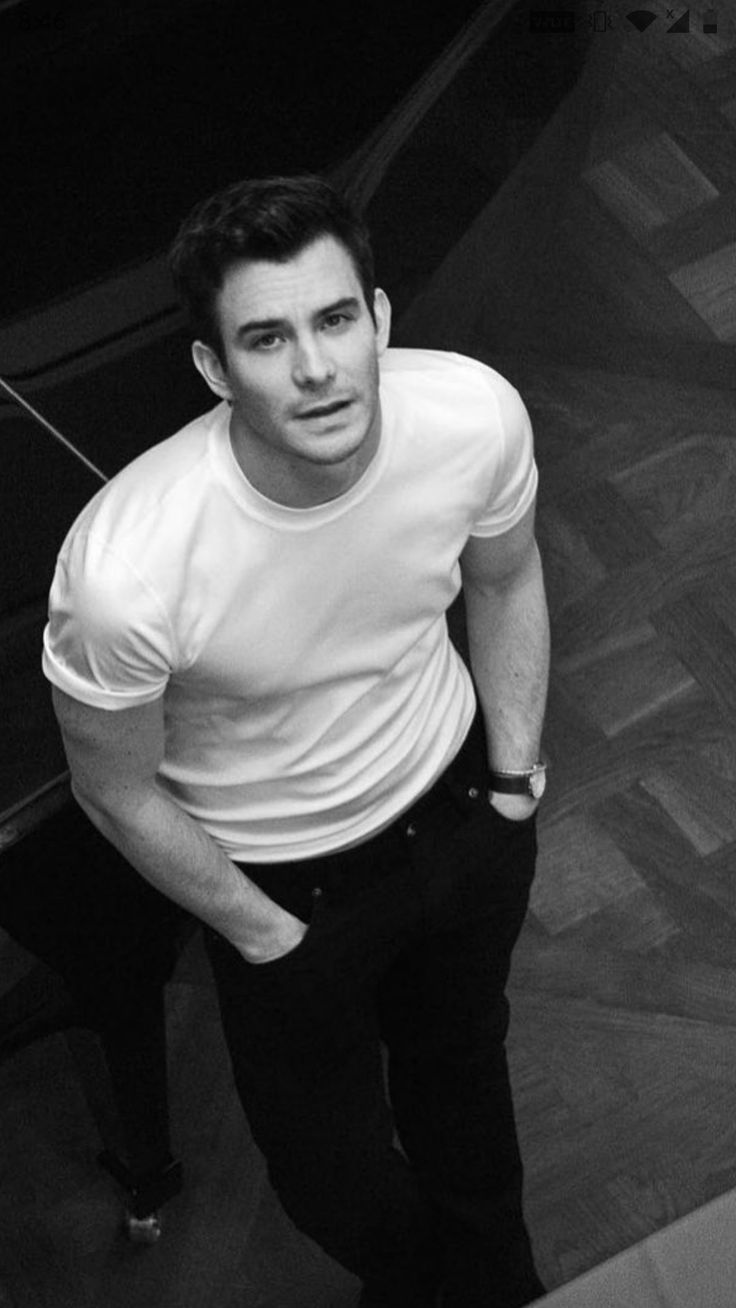 black and white photo of man in t - shirt looking down at the camera with his hand on his hip