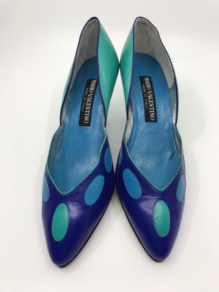 "An unworn pair of Mario Valentino heels from 1980s.  The front is bright blue with light blue and sea green oval shapes. The back and heel are sea green. They are lined with suede and silver leather with a blue leather inner sole.  Size EU 7.5B Heel height 3\"/8 cm These are in very good condition with some light mottling on the sea green leather at the back as photographed. The heel tips are chipped." Retro Blue Heels With Round Toe, Blue Pointed Toe Court Shoes With Sculpted Heel, Retro Green Leather Heels, Retro Blue Heels For Spring, Green Leather Retro Heels, Blue Retro Heels For Spring, Blue High Heel With Leather Sole, Blue Heels With Leather Sole For Evening, Blue Heels With Leather Sole And Round Toe