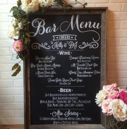 a chalkboard menu sign with flowers and greenery in front of a brick wall