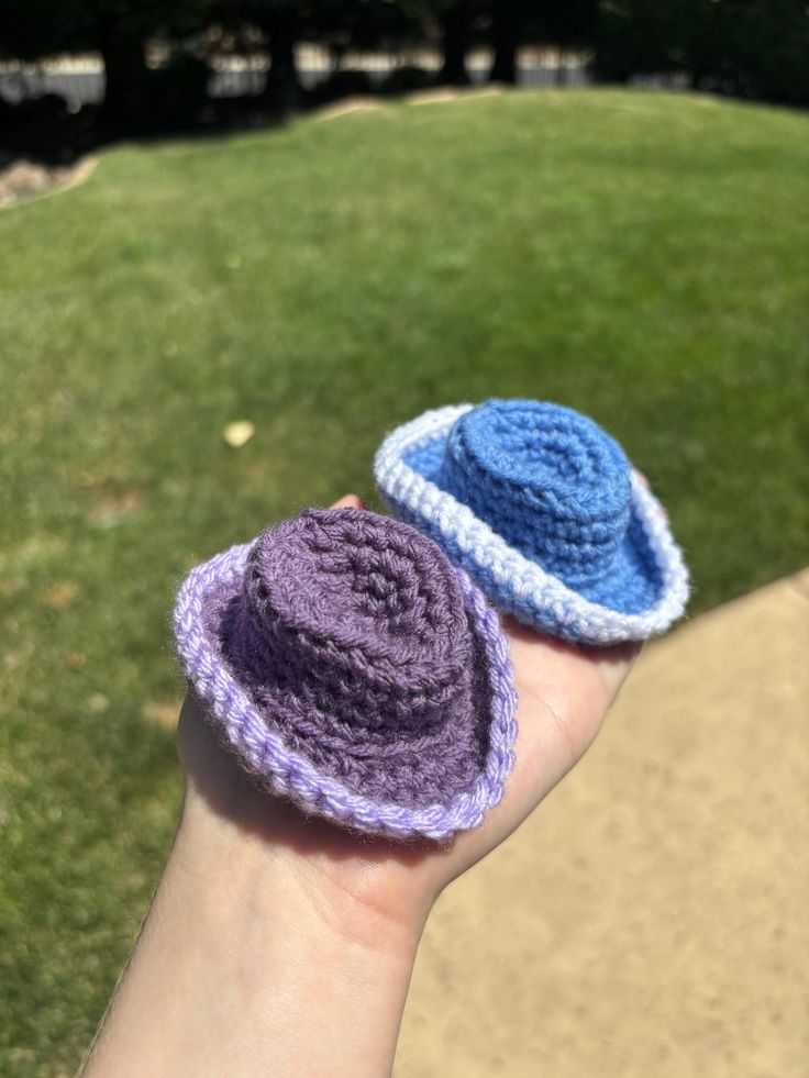 two crocheted hats sitting on someone's hand in front of some grass