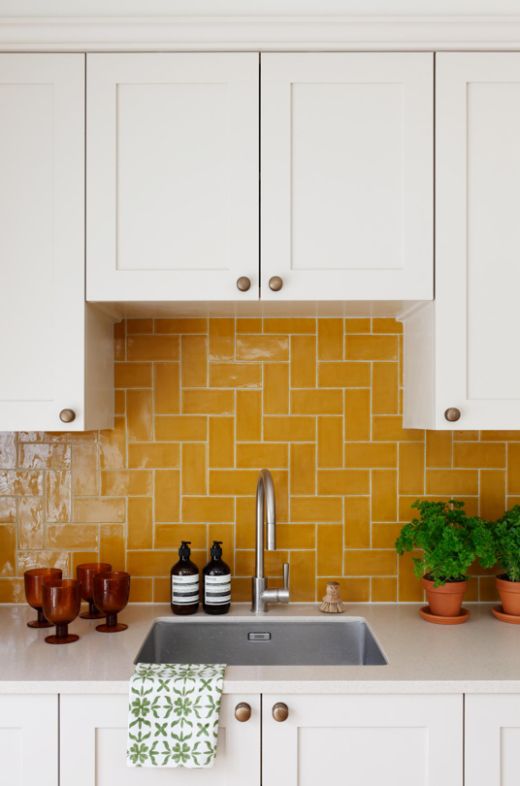 a kitchen with white cabinets and yellow tiles on the backsplash is seen in this image