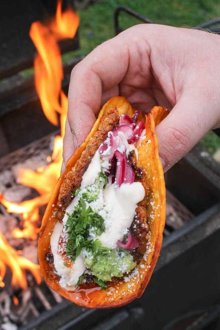 a hand holding up a pita over an open fire with vegetables and sauce on it