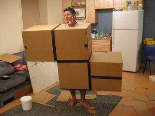 a man is standing on cardboard boxes in the middle of a living room with his head sticking out