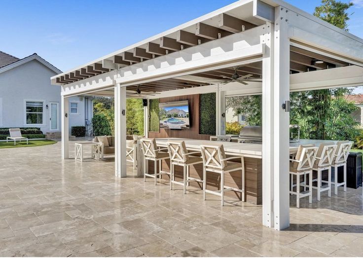 an outdoor bar with chairs and tables under a white pergolan roof in front of a house