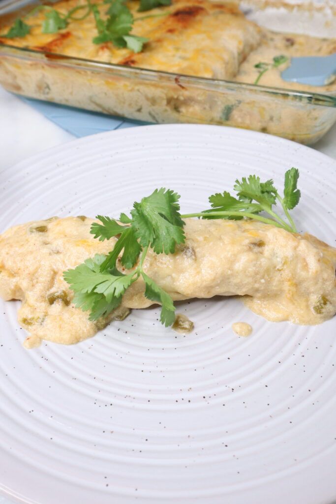 a white plate topped with an enchilada covered in cheese and cilantro