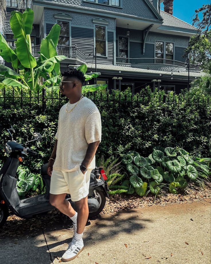 a man standing next to a scooter in front of a house with plants