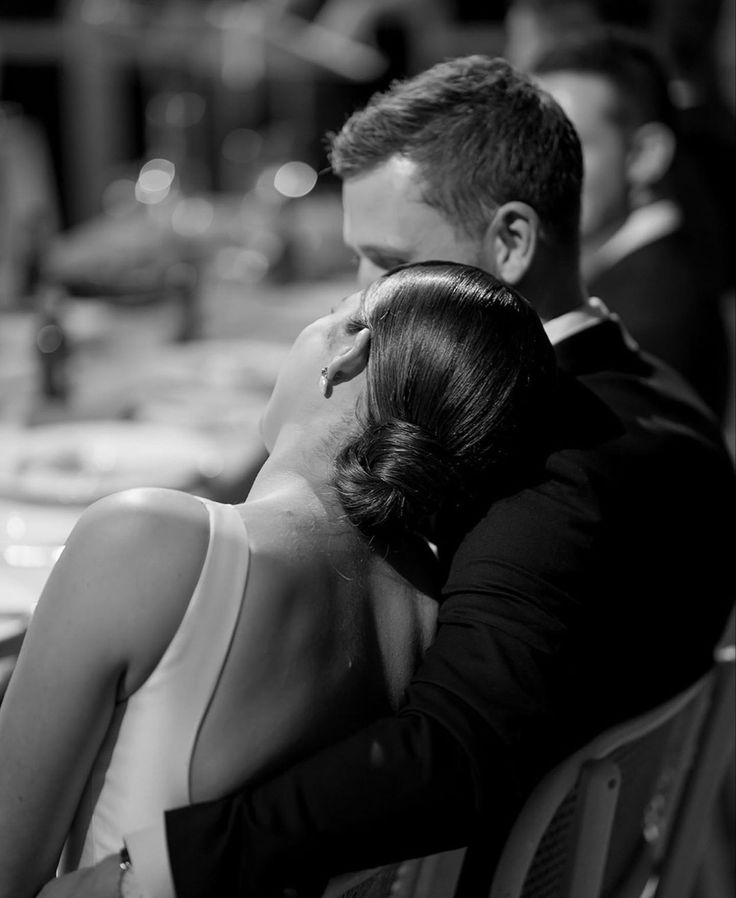 a man and woman sitting next to each other on a bench in black and white