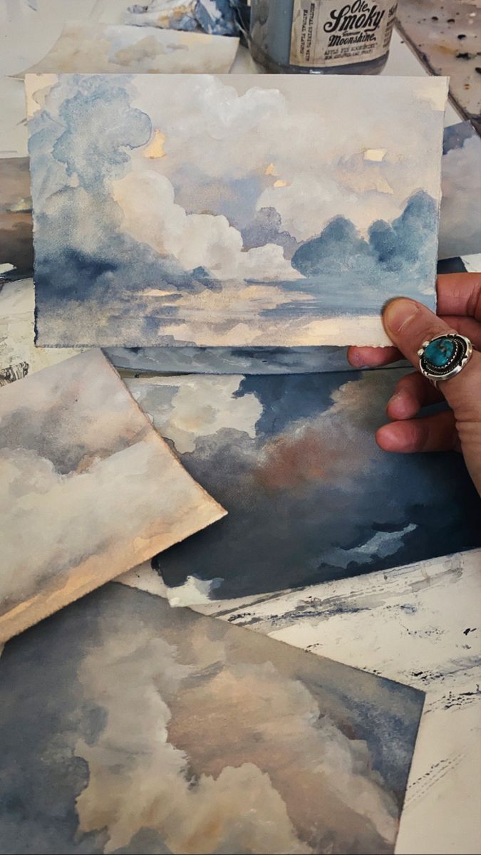 a person is painting clouds with watercolors on the table and in front of them