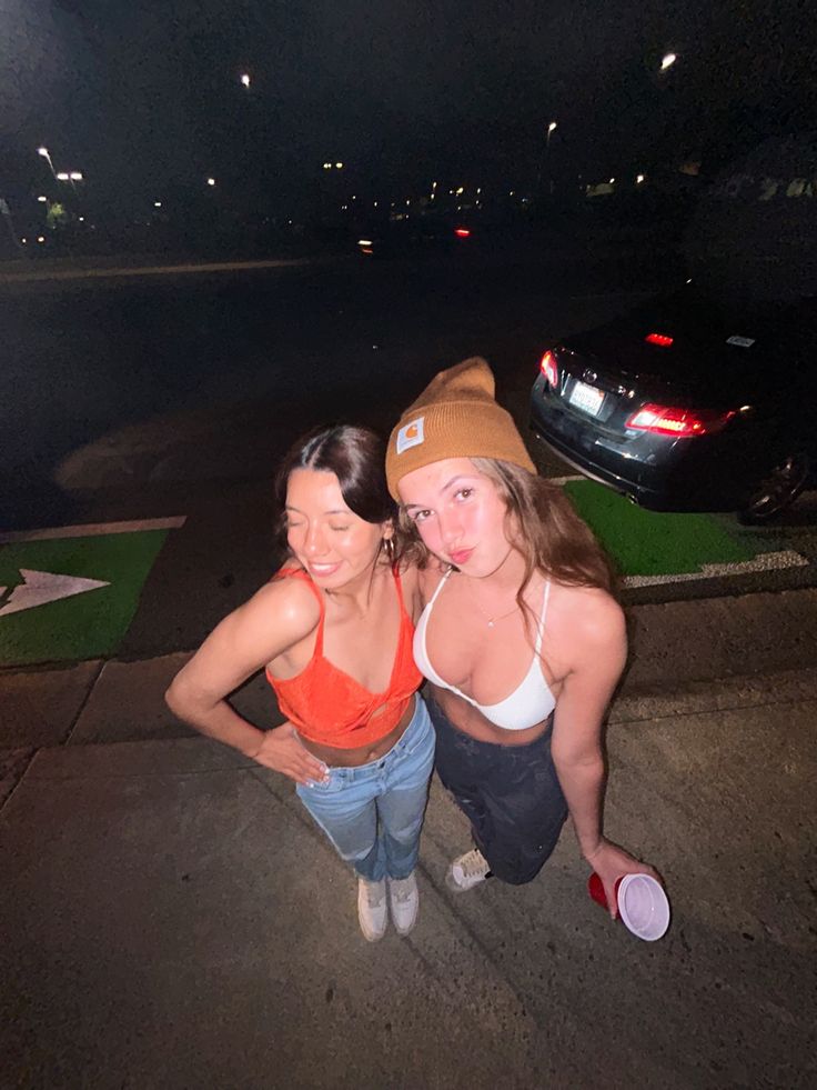 two women standing next to each other in front of a parking lot at night time