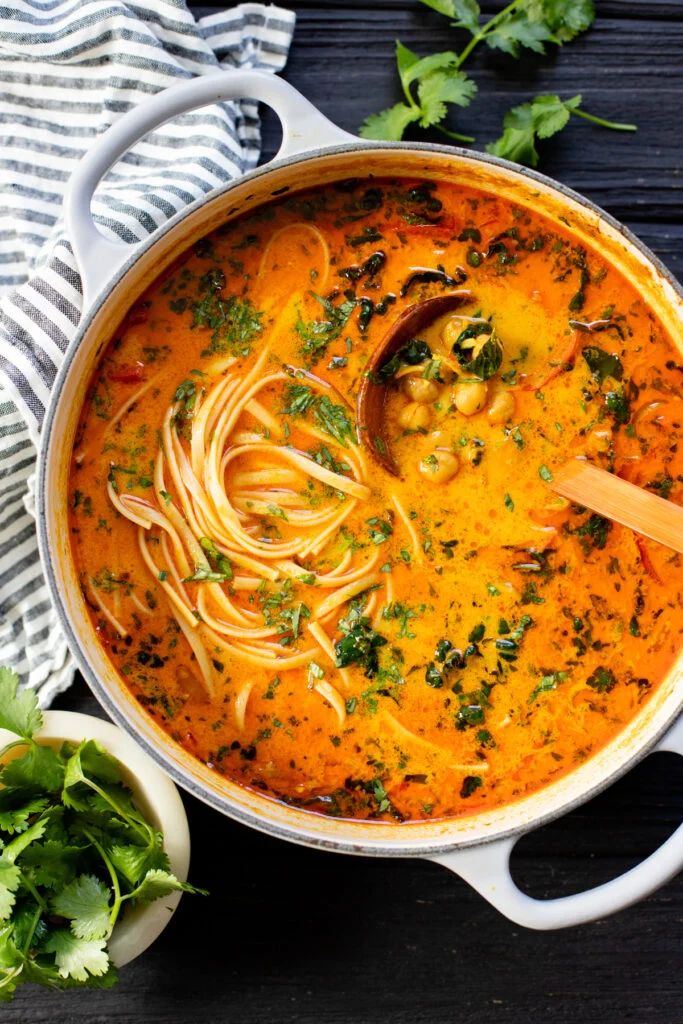 a pot filled with pasta and vegetables on top of a wooden table next to some parsley