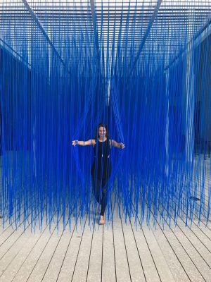 a woman standing in front of a blue structure with strings hanging from it's sides