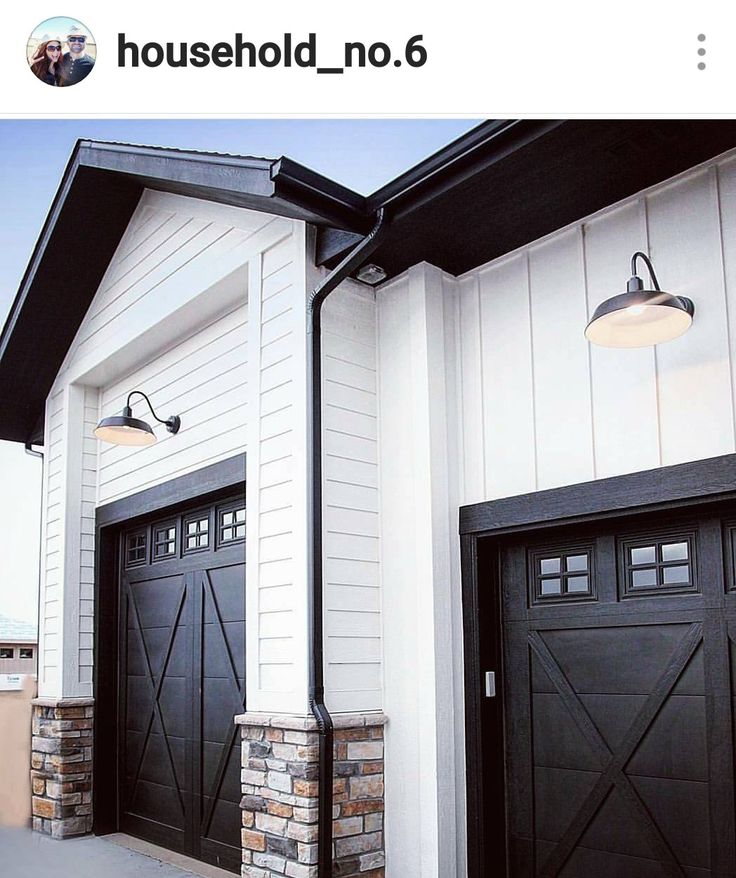 two black garage doors on the side of a white house with brick pillars and windows