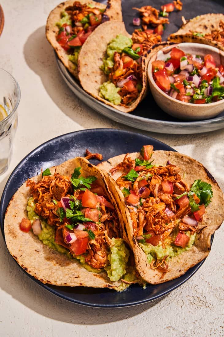 three tacos on plates with salsa and guacamole in the middle one