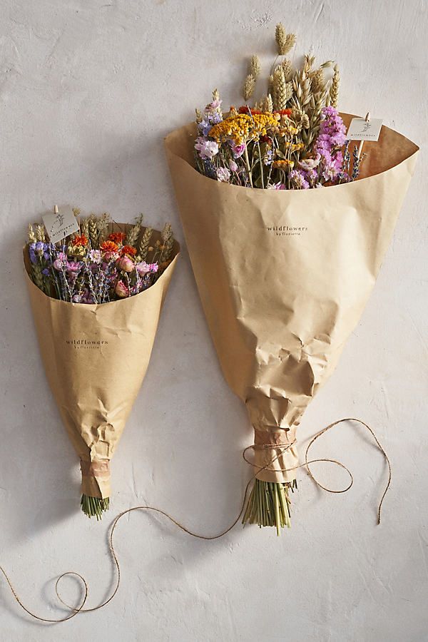 two bouquets wrapped in brown paper and tied with twine on white wall background