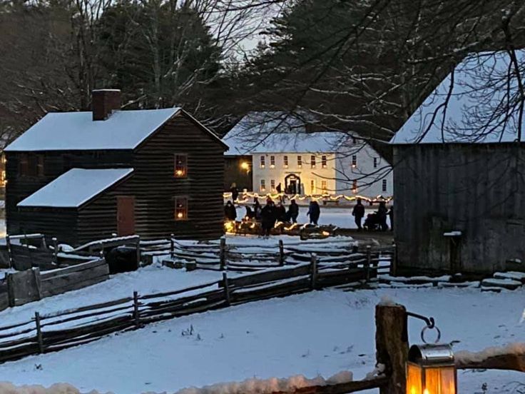 people are standing outside in the snow near some buildings and trees with lights on them