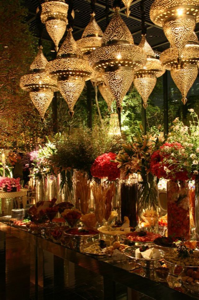 a long table covered in lots of vases filled with flowers and lights hanging from the ceiling