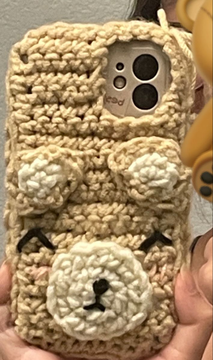 a person holding up a cell phone case made to look like a crocheted dog