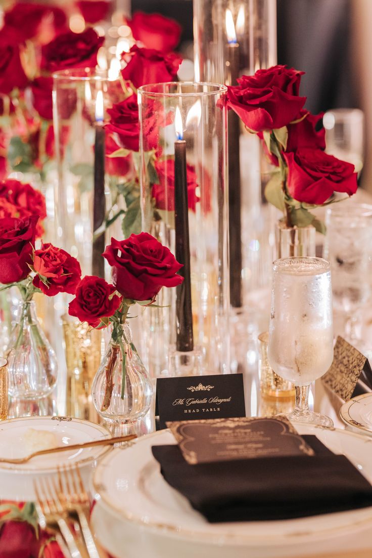 red roses in glass vases on a table with silverware and place settings for dinner