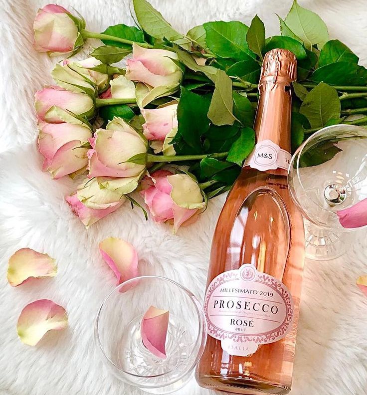 a bottle of rose wine next to two glasses and flowers on a white furnishing