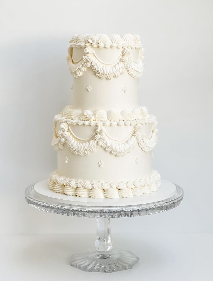 a three tiered white wedding cake sitting on top of a glass platter next to a wall