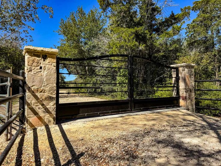 a gated in area with stone walls and iron gates leading into the woods on a sunny day