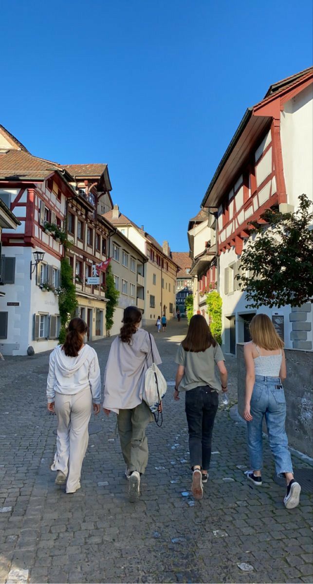 three women are walking down the street in front of some buildings and one is carrying a purse