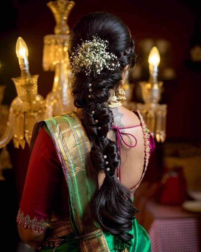 a woman with long hair wearing a green and red saree, standing in front of chandelier