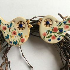 two ceramic birds sitting next to each other on top of some twigs with flowers and leaves