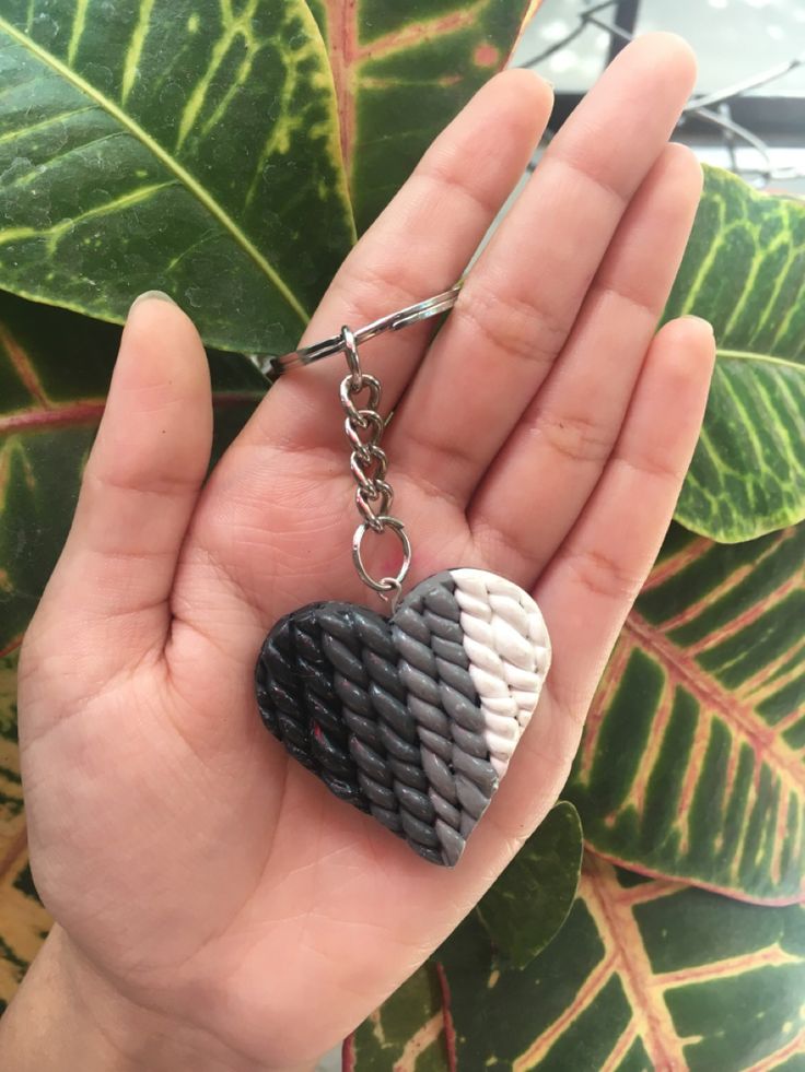 a hand holding a heart shaped keychain in front of a leafy plant