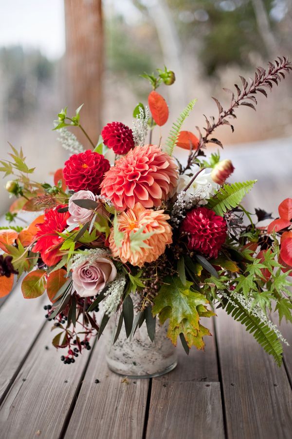 a vase filled with lots of flowers sitting on top of a wooden table next to trees