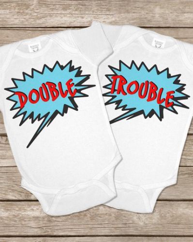 two white onesuits with the words double trouble printed on them, sitting next to each other