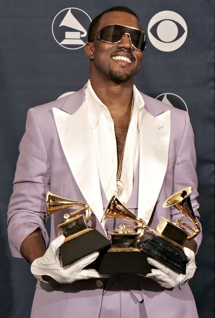 a man in a purple suit and sunglasses holding two awards at the same time as he smiles