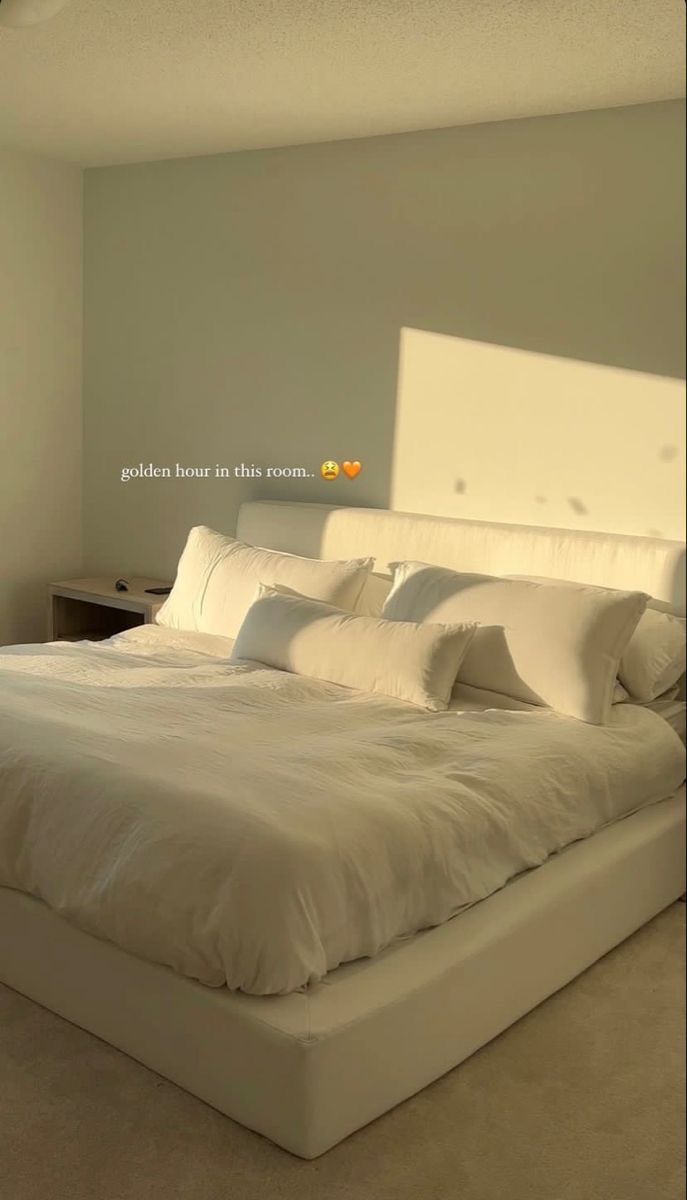 a large bed with white sheets and pillows in a room that has light colored walls