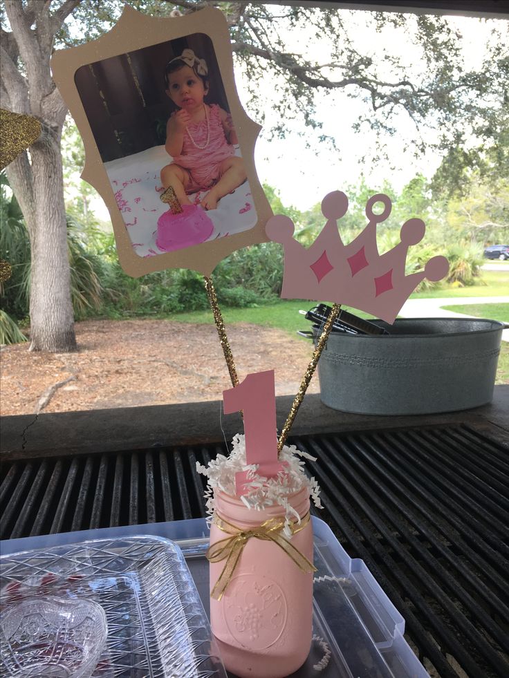 a pink mason jar filled with baby's first birthday decorations on top of a grill