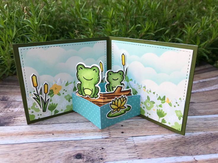 two cards with frog images on them sitting next to each other in front of some plants