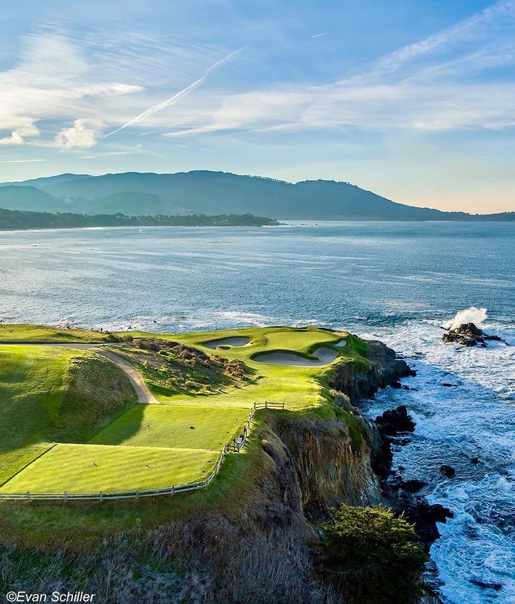 an aerial view of a golf course near the ocean with mountains in the background and blue sky