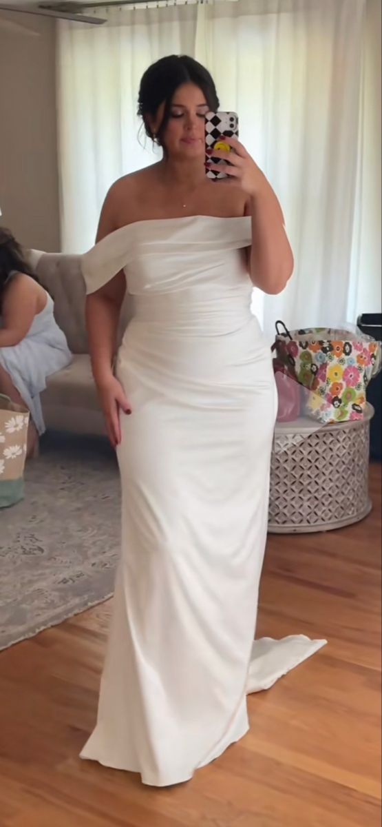 a woman in a white dress taking a selfie with her cell phone while standing on a hardwood floor