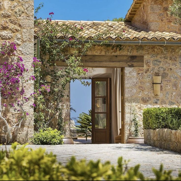 an entrance to a stone building with flowers growing on the outside wall and doors open