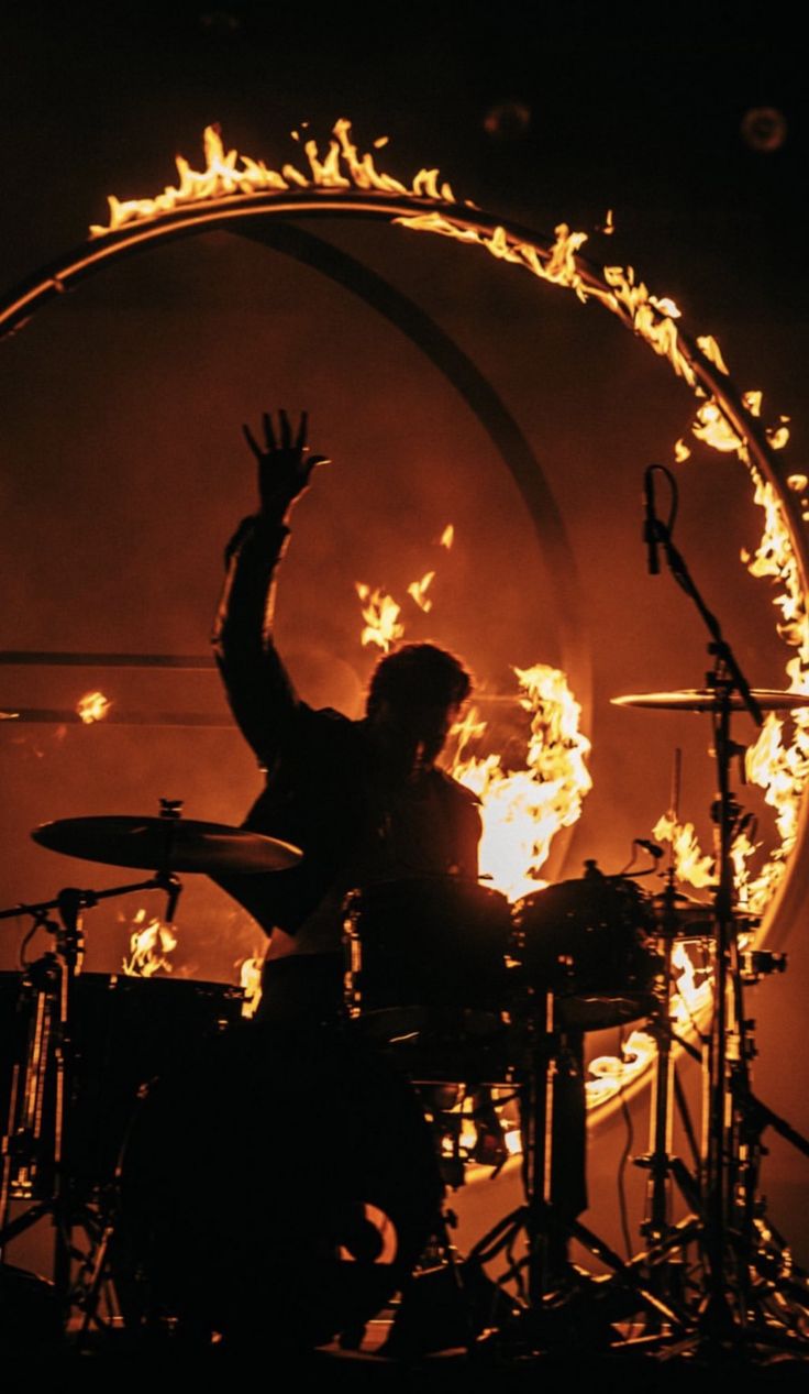 a man on stage with his hands up in the air and fire behind him,