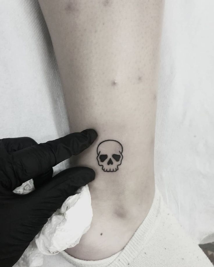 a person with a skull tattoo on their left side of the arm, holding onto another hand