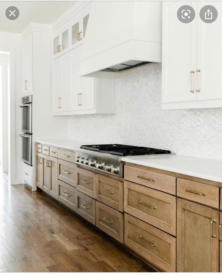 a kitchen with white cabinets and wood flooring, an oven and stove hood is shown