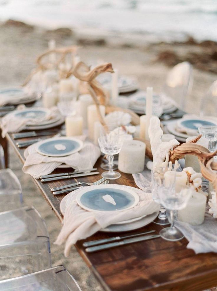 a long table set up with plates and candles on the beach for an outdoor dinner