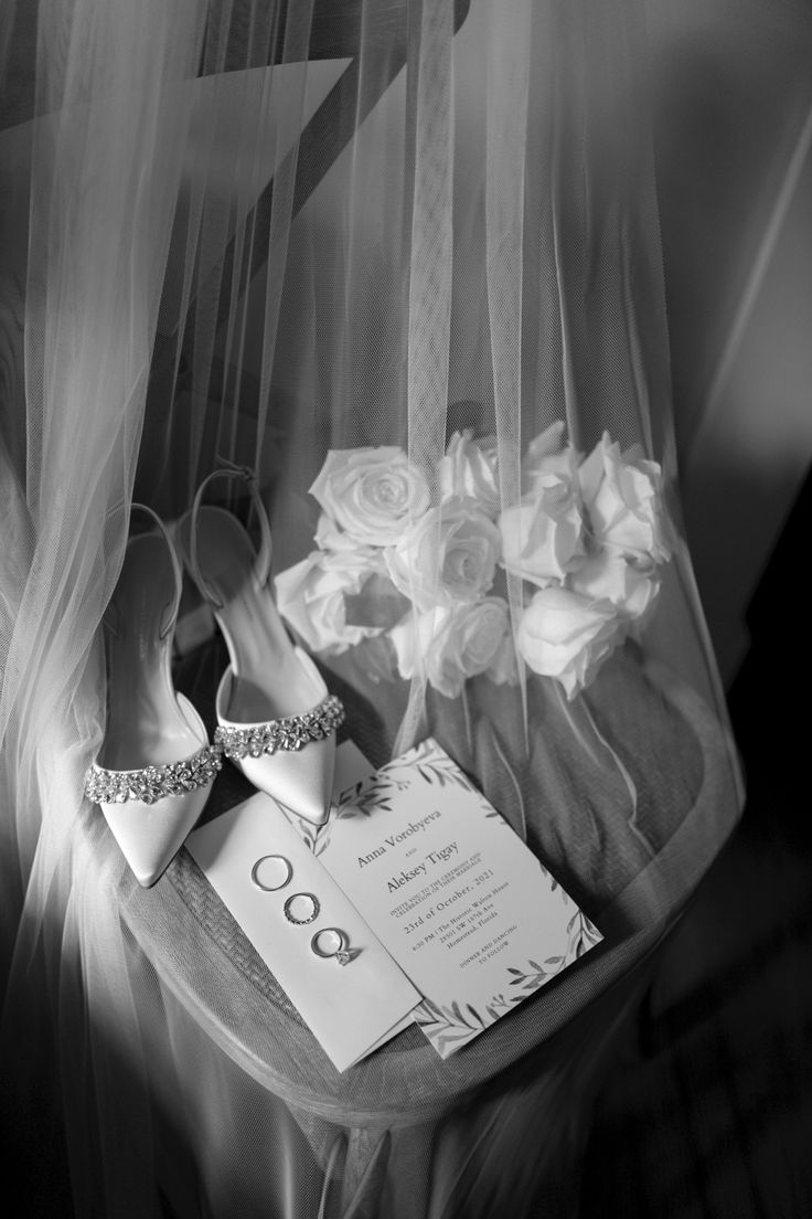 the wedding shoes are sitting on the table next to the veil and flowers in black and white