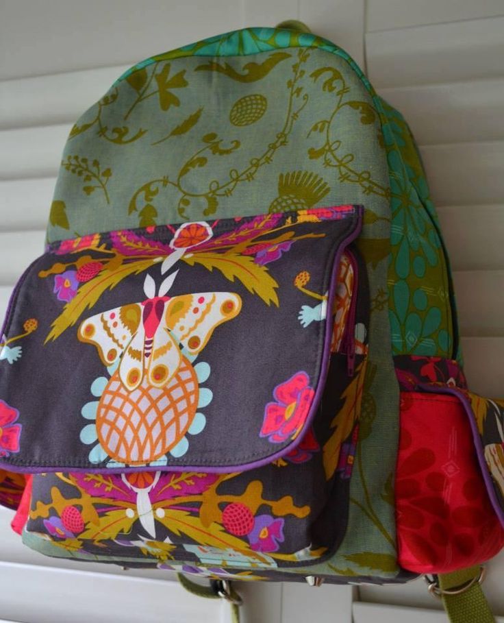 two colorful backpacks sitting on top of a white shelf in front of a window