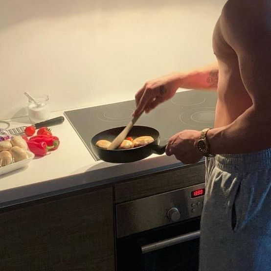 a shirtless man cooking food in a frying pan