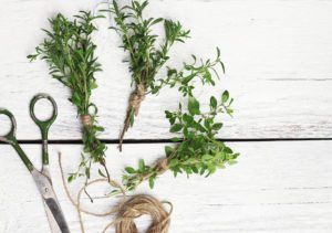 herbs and scissors on a white wooden table with twine, sprigs, and rope